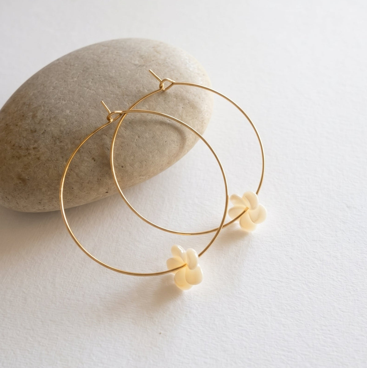 Gold hoop earrings with small carved shell plumerias.