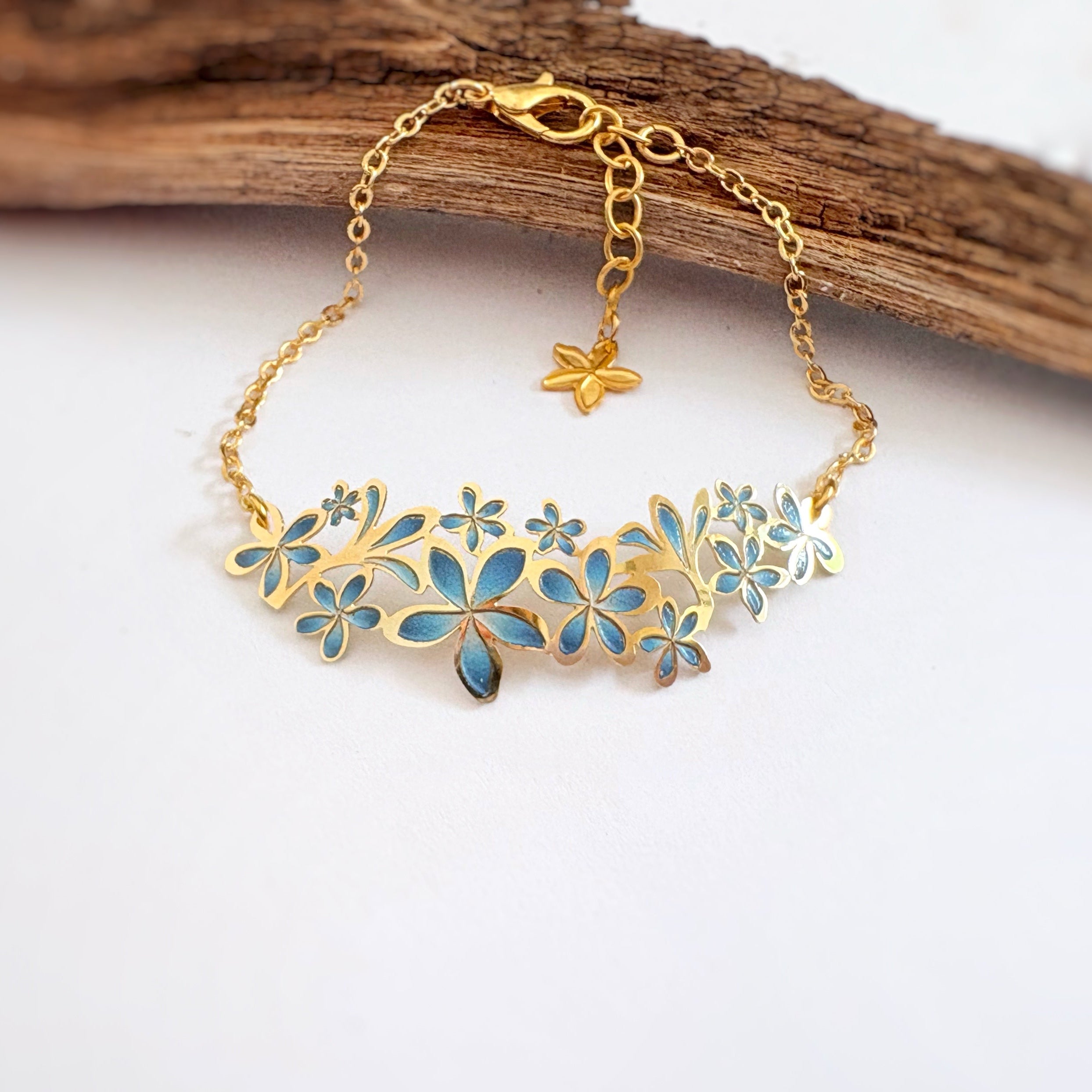 Gold bracelet with blue plumeria floral designs on a white background