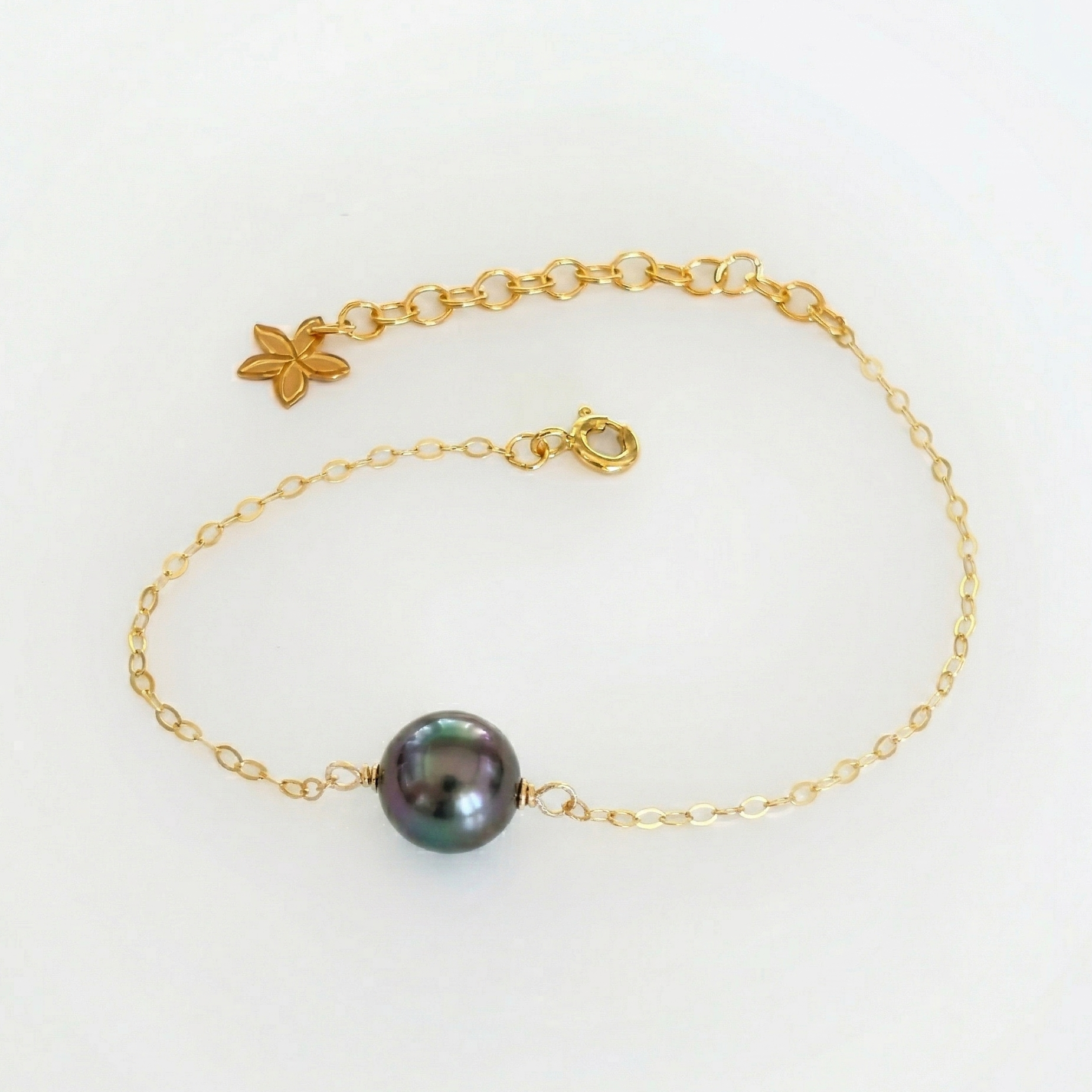 Gold tahitian pearl bracelet with a black pearl on a white background