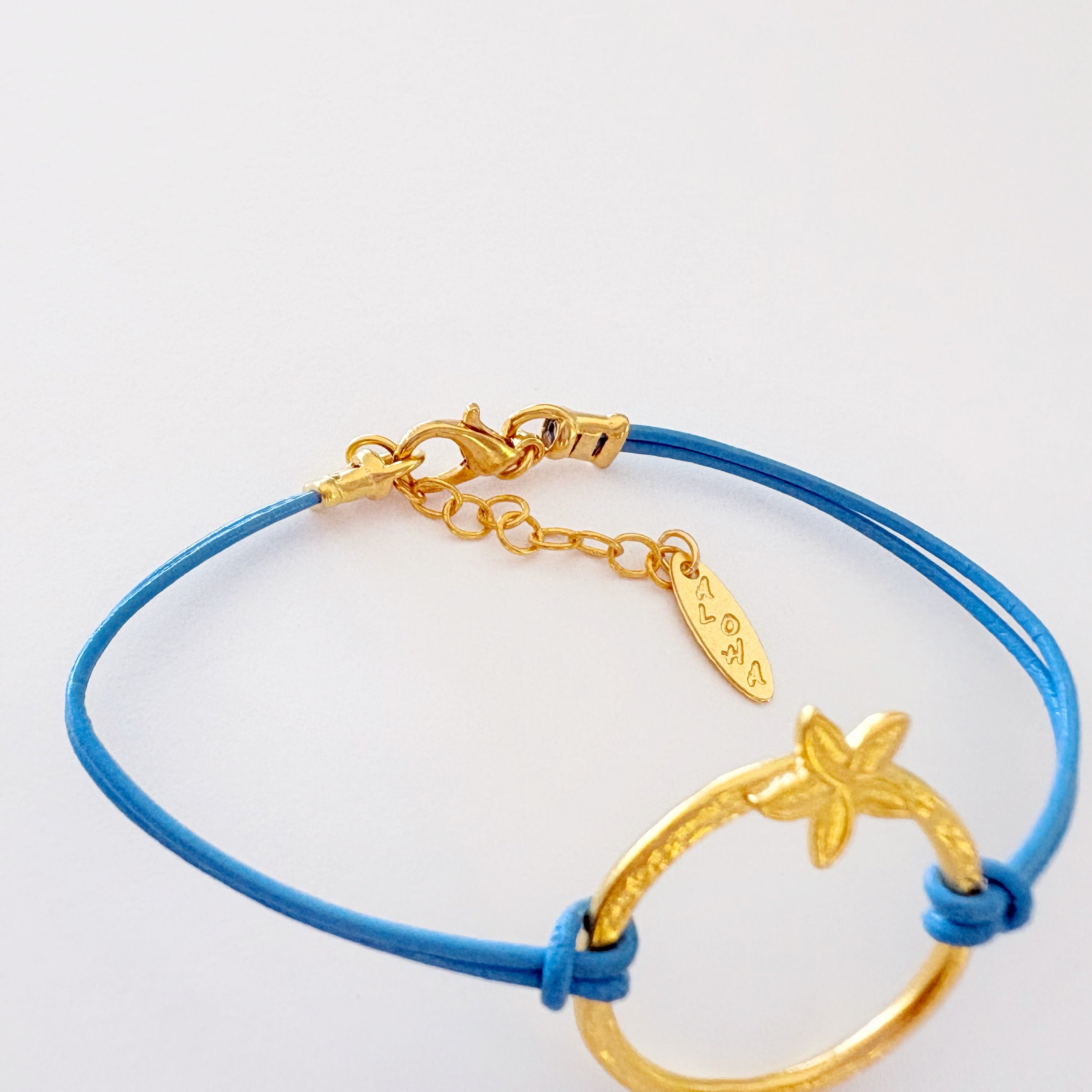 Gold bracelet with starfish charm on a blue cord against a white background