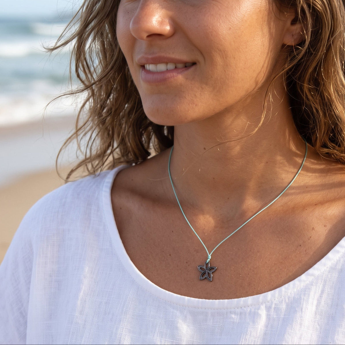 A woman on a beach wearing a delicate silver necklace with a starfish pendant, paired with a white linen top.