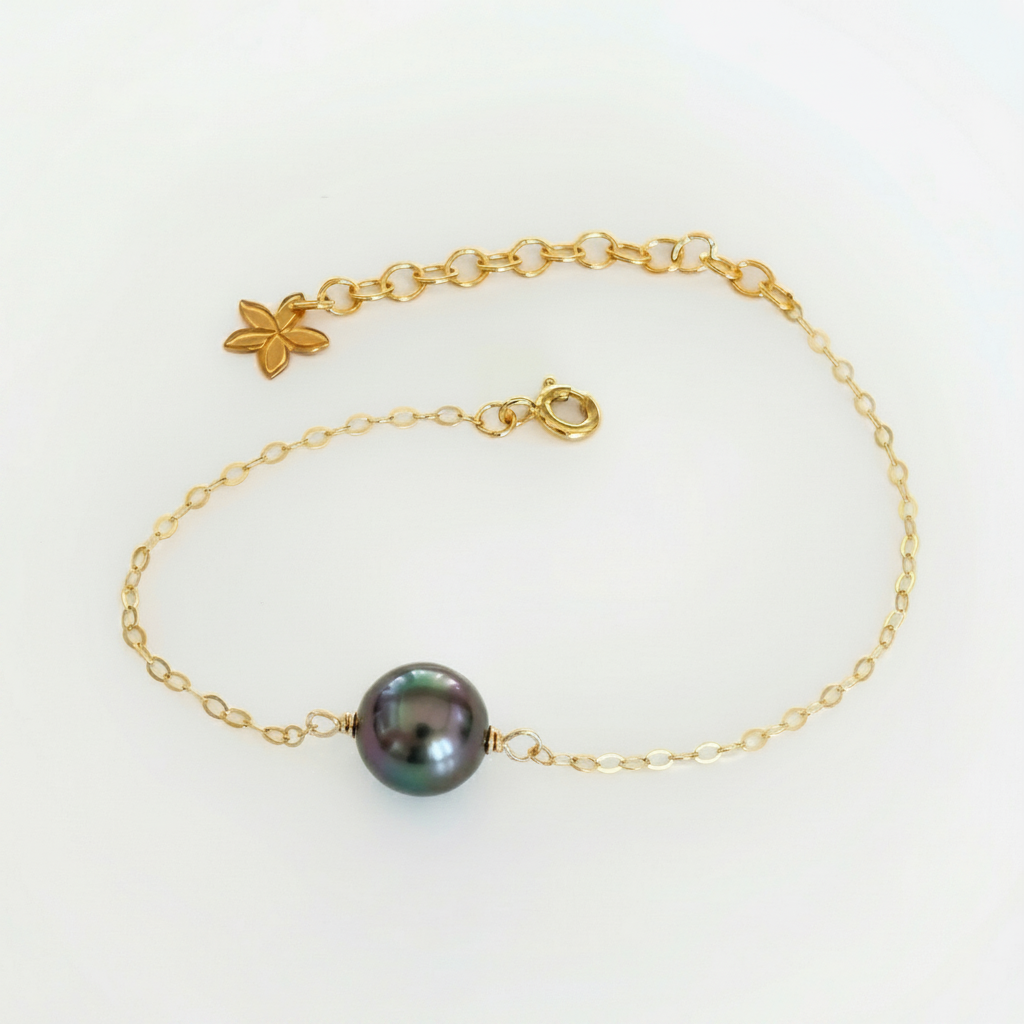 Gold tahitian pearl bracelet with a black pearl on a white background